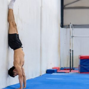 Person practicing a wall-supported handstand in a gymnastics gym