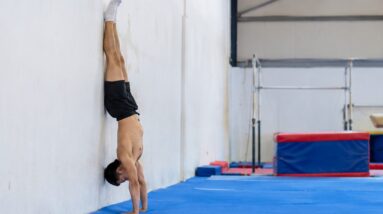 Person practicing a wall-supported handstand in a gymnastics gym