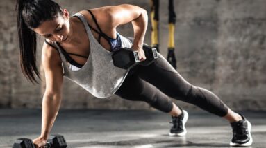 Woman doing a plank row with dumbbells, strong and focused expression during workout