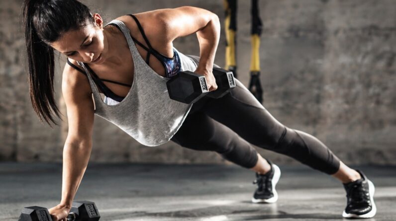 Woman doing a plank row with dumbbells, strong and focused expression during workout